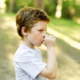 Thumb sucking blog featured image of a young boy sucking his thumb outdoors.